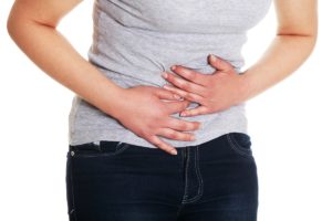 Pessoa com as mãos sobre o abdômen indicando dor ou desconforto intestinal.